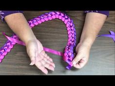 two hands holding purple and pink ribbon in the shape of a heart on top of a wooden table