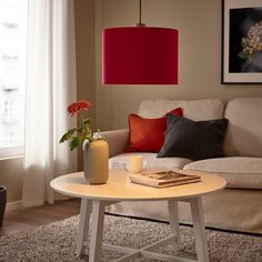 a living room with a couch, coffee table and red lampshade in the corner