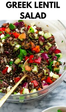 greek lentil salad in a glass bowl with a wooden spoon and serving utensils