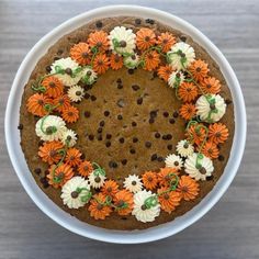 a cake decorated with orange and white flowers on top of a wooden table in a bowl