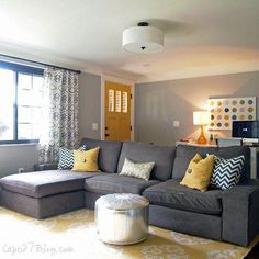 a living room with gray couches and yellow pillows on the floor in front of a large window