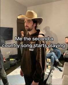 a man wearing a cowboy hat standing in front of a couch with people sitting around