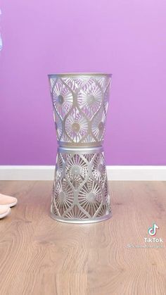 a vase sitting on top of a wooden floor next to a purple wall and white shoes