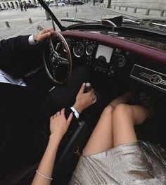 a man and woman sitting in the driver's seat of a car, with their hands on the steering wheel