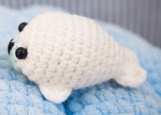 a small white stuffed animal laying on top of a blue blanket with black eyeballs