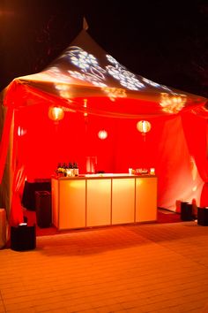 a red tent with lights on it and some stools in front of the bar