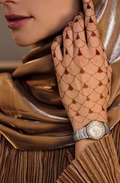 a woman with henna on her hand is wearing a gold dress and a watch