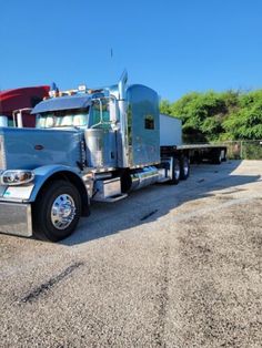 a blue semi truck parked in a parking lot next to a red and white trailer