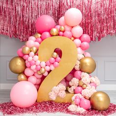 the number two is surrounded by balloons and streamers in pink, gold and white