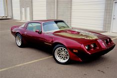 a red sports car parked in front of a garage door with gold emblems on the hood