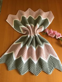 a crocheted blanket sitting on top of a wooden table next to a pink flower