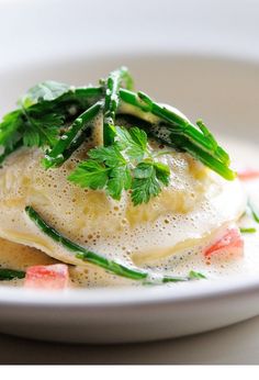 a white plate topped with ravioli covered in sauce and garnished with parsley