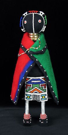 an african doll is standing with his arms crossed and wearing a colorful coat, headdress, and red shoes