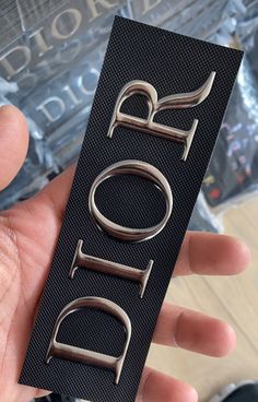 a hand holding a black and silver metal name tag with the word riot on it