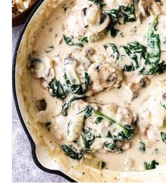 a skillet filled with chicken and spinach covered in white sauce next to pasta