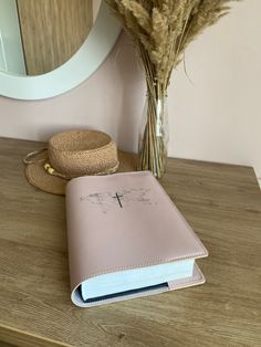 a pink book sitting on top of a wooden table next to a vase with dried flowers