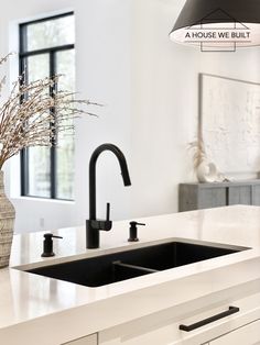 a white kitchen with two black faucets and a large vase on the counter