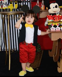 a little boy standing in front of a mickey mouse cake