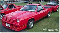 two red sports cars parked next to each other on the grass in a parking lot