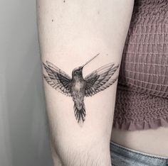 a small hummingbird tattoo on the left inner arm and upper arm, with its wings spread out