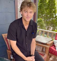 a young man is sitting on a chair and looking at the camera while wearing a black shirt