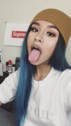 a woman with blue hair sticking her tongue out and making a funny face while wearing a beanie