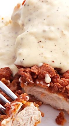 a white plate topped with meat covered in gravy and mashed potatoes next to a fork