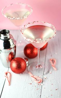 two martinis with candy canes in front of them on a white wooden table