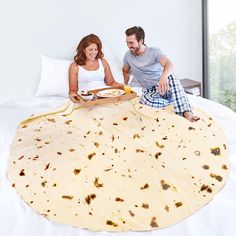 a man and woman sitting on top of a bed with food in front of them