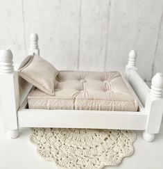 a small white bed with pillows on top of it and a doily mat underneath