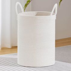 a large white basket sitting on top of a wooden floor next to a potted plant