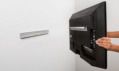 a woman is holding up a television screen to the wall with her hand on it