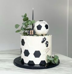 a white and black cake with a soccer ball on top, surrounded by greenery