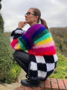 a woman sitting on top of a brick wall wearing a colorful sweater and black leather pants