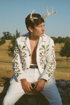 a man sitting on top of a rock wearing a white suit with antlers on his head