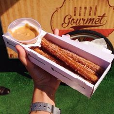 a person holding up a box of churros with dipping sauce in it's hand