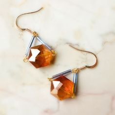 the earrings are made from gold and silver wire with an orange faceted glass bead