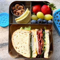 a lunch box with a sandwich, fruit and nuts