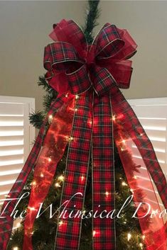 the christmas tree is decorated with red and black plaid ribbon, lights, and a bow