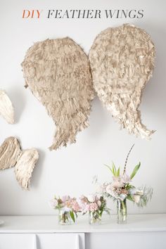 two angel wings hanging on the wall next to vases with flowers in front of them