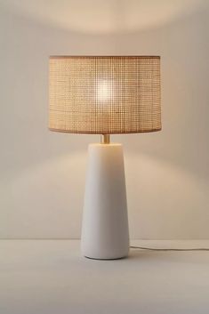 a white table lamp with a beige shade on it's base and a light bulb in the middle