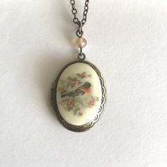 "Here is a pretty bird locket necklace. This necklace features an oval shaped brass locket with a vintage style cameo cabochon in the center. The cabochon depicts a sweet spring robin bird perched on a cherry blossom branch, the cameo is made from resin. This locket has an engraved floral pattern along the front side border and it is suspended from a glass bead. Locket comes on a sturdy soldered brass chain that is closed with a solid brass clasp. Perfect for spring or summer. All jewelry comes in a Botanical Bird gift box, perfect for gift giving or for a gift for yourself! Locket measures: 7/8\" across x 1.25\" long Necklace chain length - please choose from the drop down menu. Check out more Botanical Bird Jewelry here: www.etsy.com/shop/BotanicalBird" Bird Locket, Robin Necklace, Locket Vintage, Side Border, Victorian Locket, Blossom Branch, Cherry Blossom Branch, Robin Bird, Bird Gifts