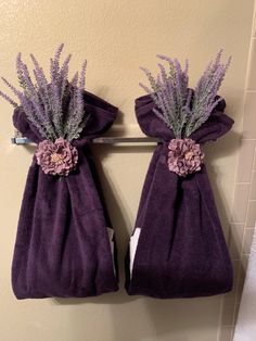 two purple towels are hanging on the wall with flowers in them and one towel has been folded over it