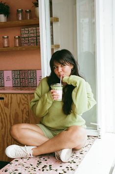 a woman sitting on the floor drinking from a cup with a straw in her mouth