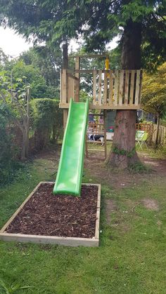 a green slide sitting in the grass next to a tree