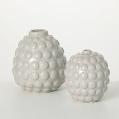 two white vases sitting next to each other on top of a table with a white wall in the background