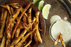 some french fries are on a plate next to a glass of ranch dressing and lime wedges