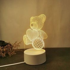 a light up teddy bear sitting on top of a white stand next to a plant