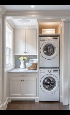 a washer and dryer in a white laundry room with cabinets on either side