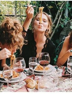 three women sitting at a table with wine glasses and food in front of their faces